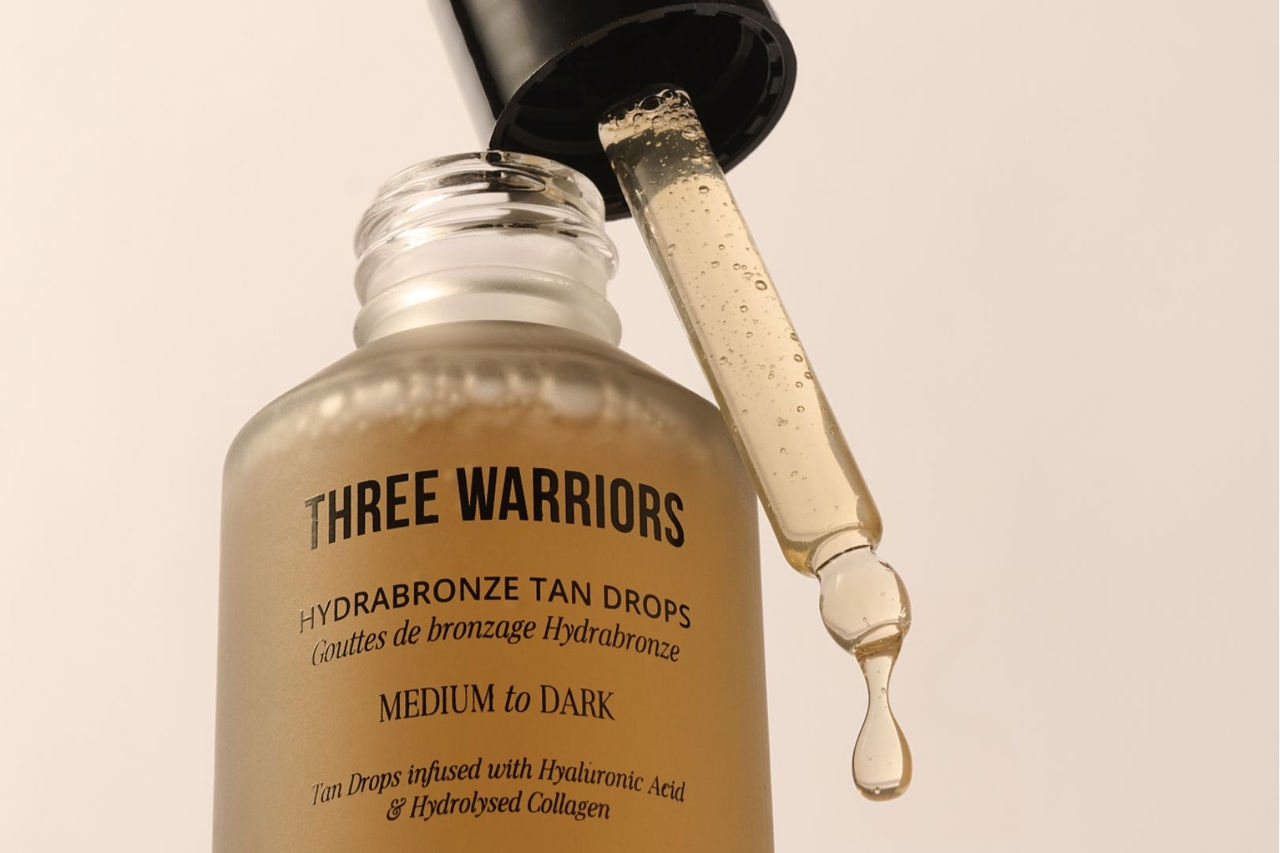 a small glass bottle with a light, brown coloured liquid sits alongside an eyedropper with a drop of the liquid dripping out