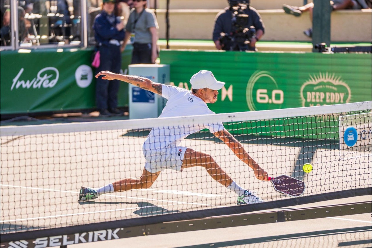 A man slides on a pickleball court near the net to reach the ball with his paddle