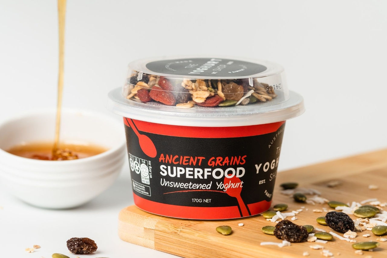 honey drizzling down from a spoon into a small white bowl next to a sealed yoghurt container