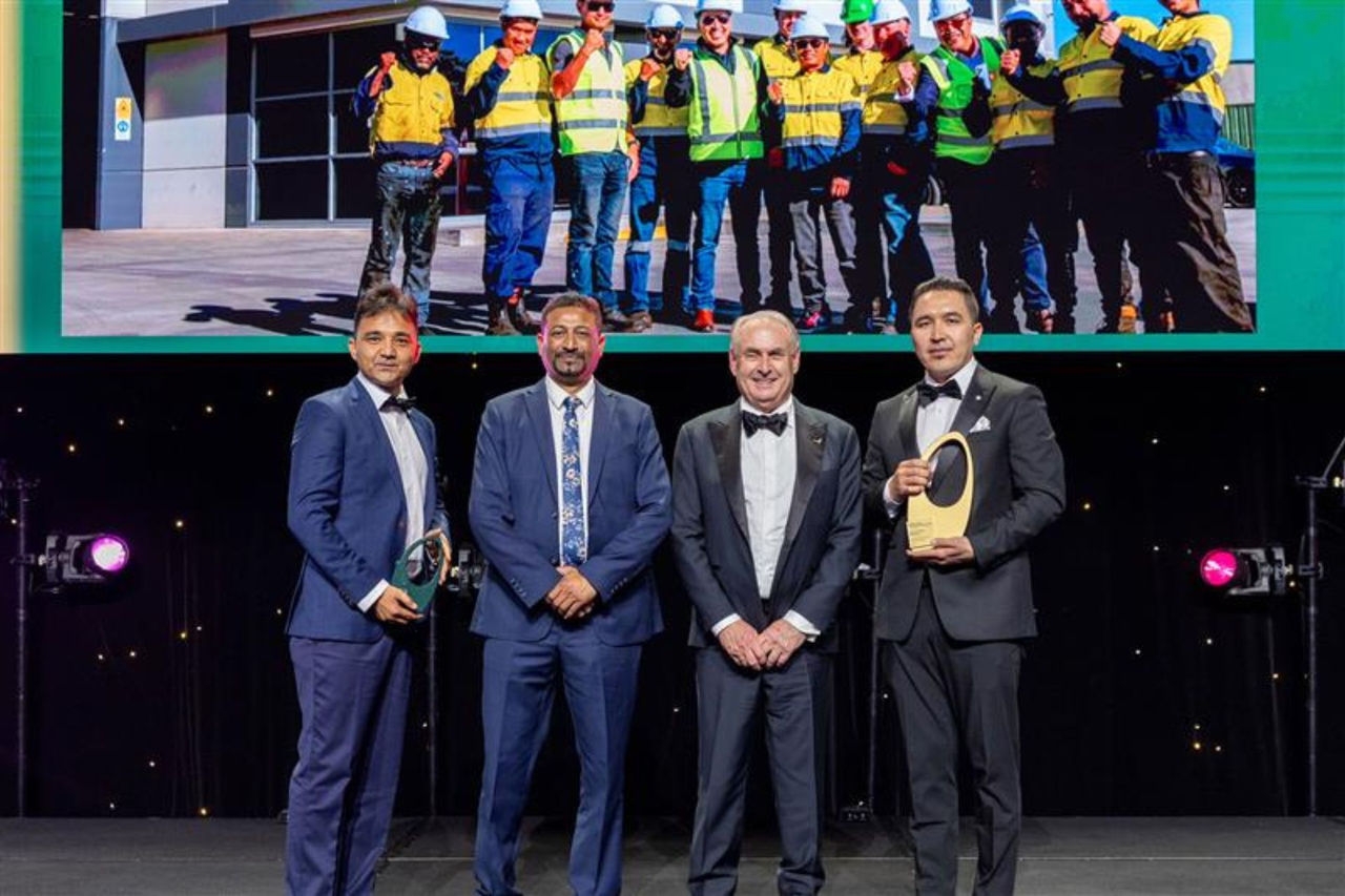 Four men on stage for an award's presentation with the man on the right holding a gold award