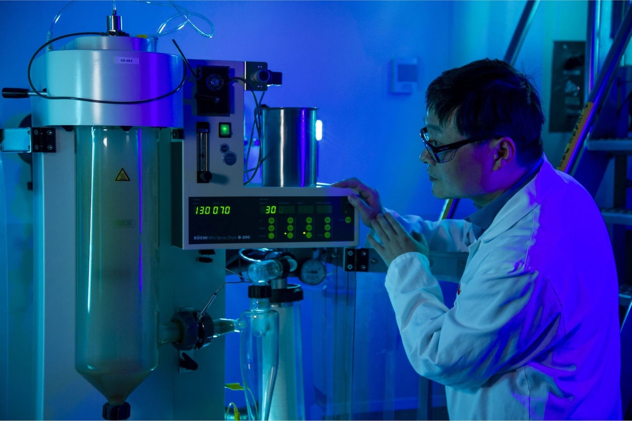 a technician in a white lab coat looks at a machine in a lab under dim blue light