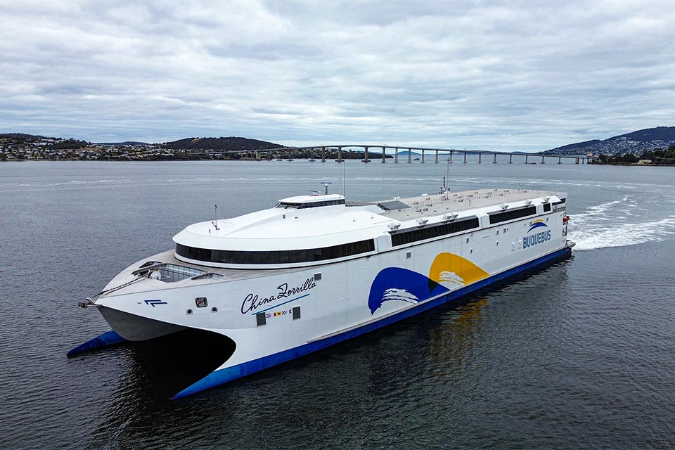 Incat vessel on large waterway with city and bridge in the background