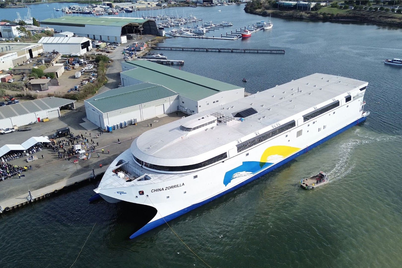 a large white catamaran ship in the water next to a wharf with people attending a launch ceremony