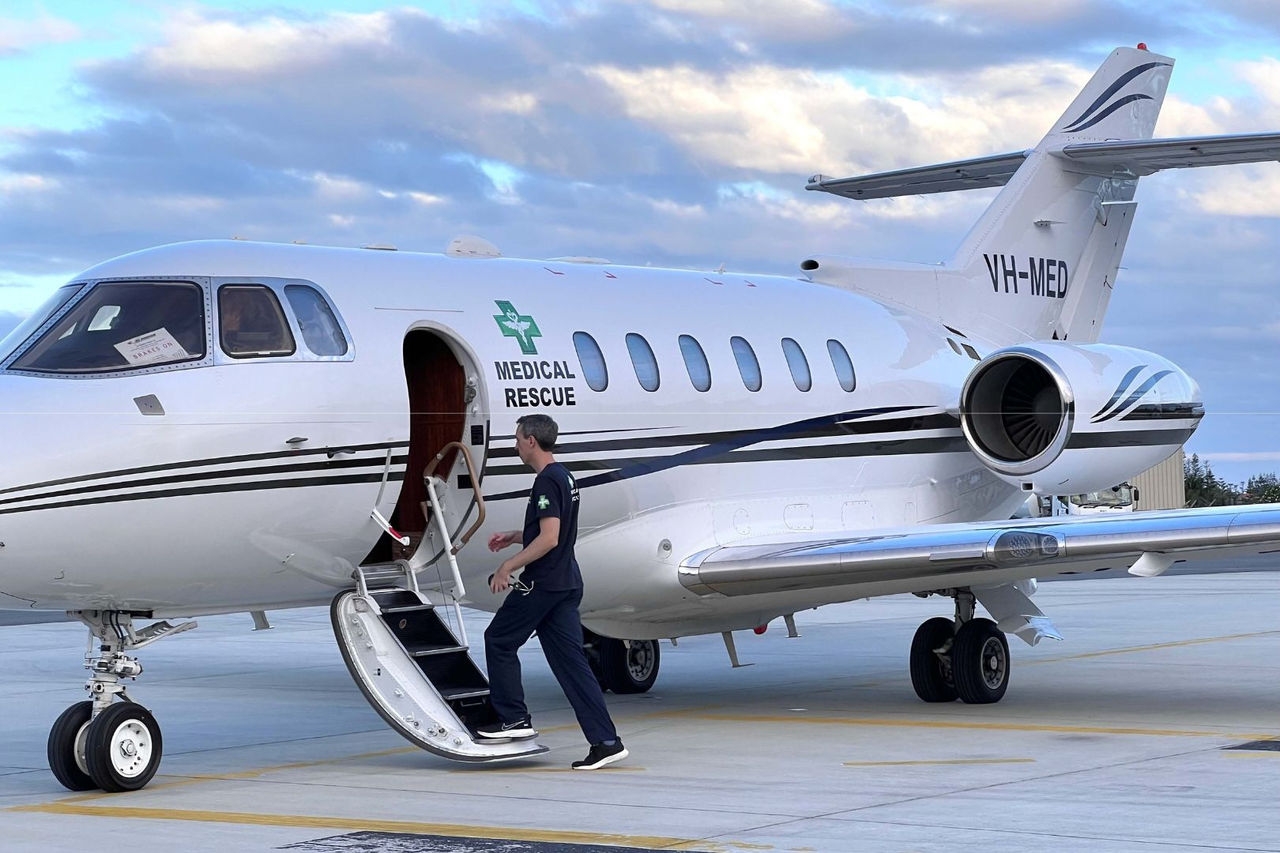 a male medical person boards a light jet aircraft parked on an airport apron