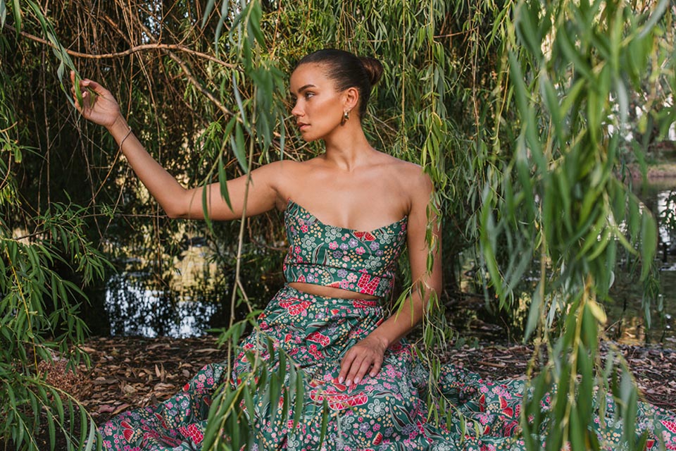 Woman sitting in green and pink pattern dress with willow tree in the background