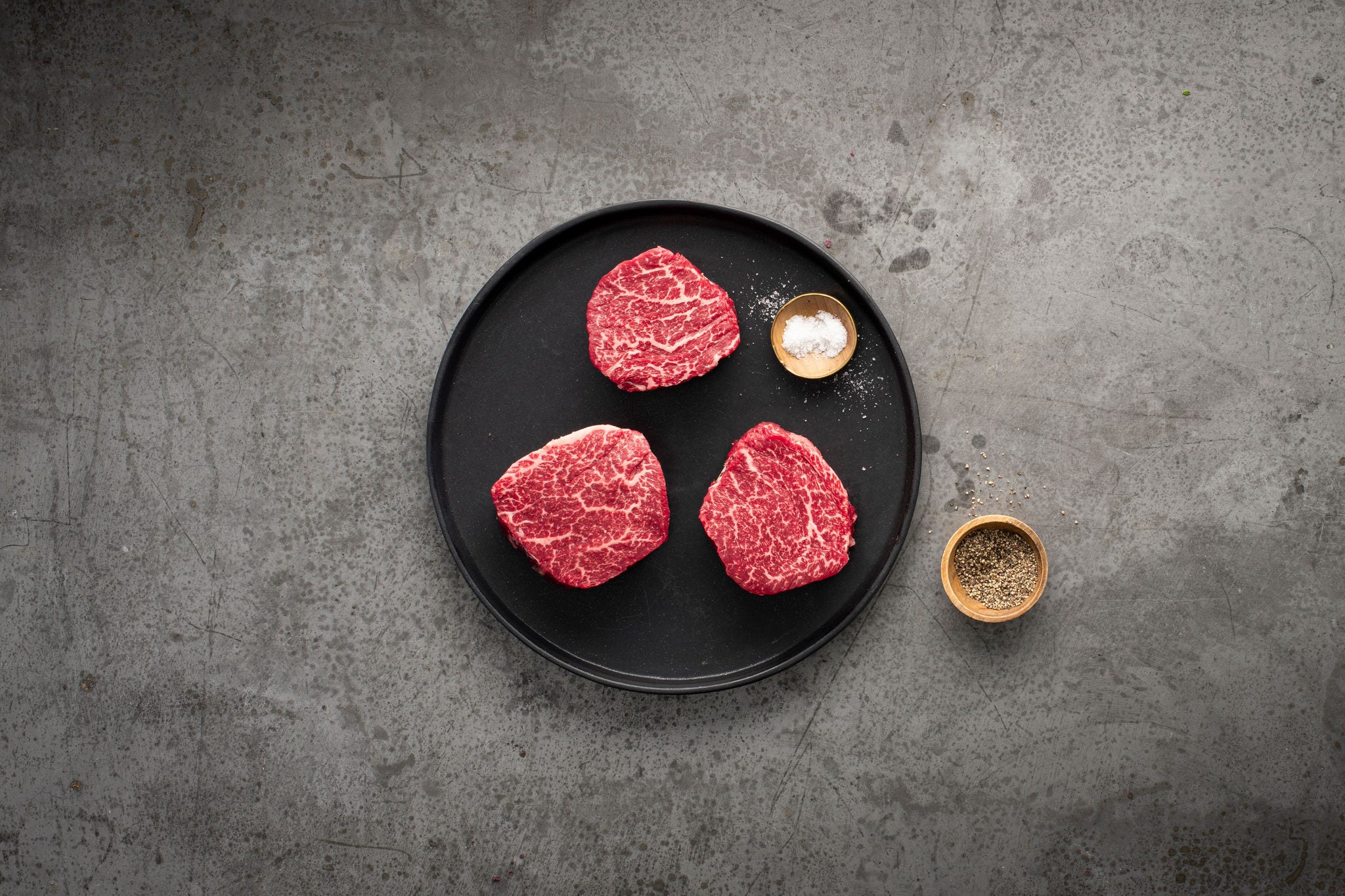three raw steaks on a plate with salt