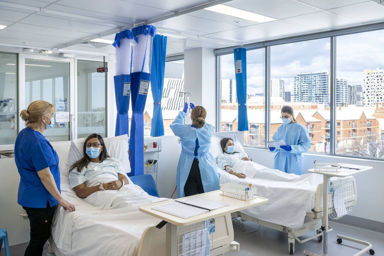 medical staff check on a patient who is lying down in a hospital bed