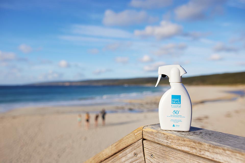 Bottle of spray sunscreen on a wooden railing at a beach