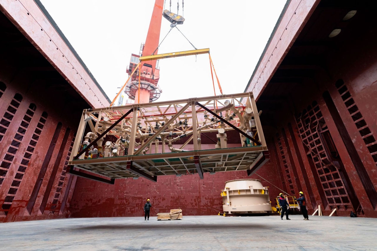 a crane lowers a rectangular steel frame containing equipment into a ship's hold