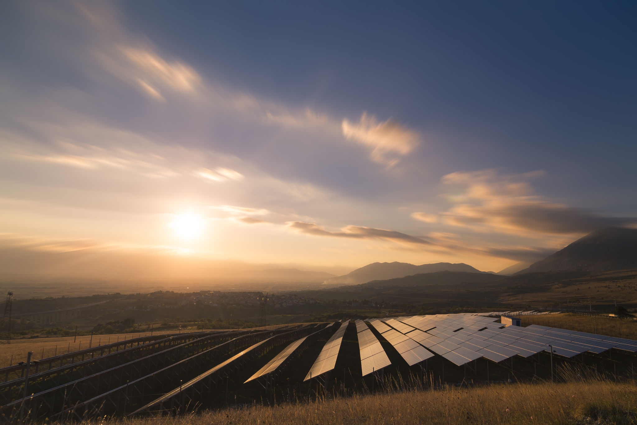 Landscape picture of a solar plant that is located inside a valley surrounded by mountain during the sunset.