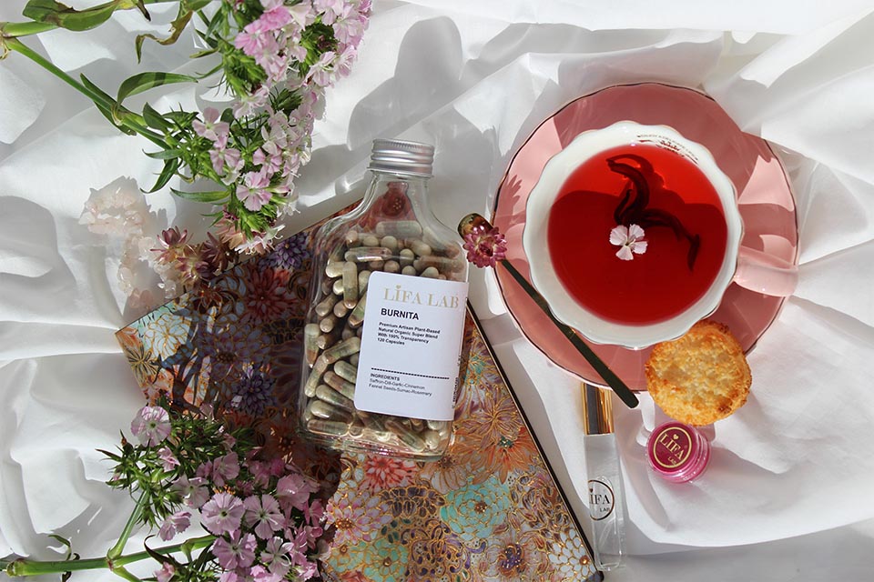 Glass bottle containing capsules, teacup filled with red liquid and flowers