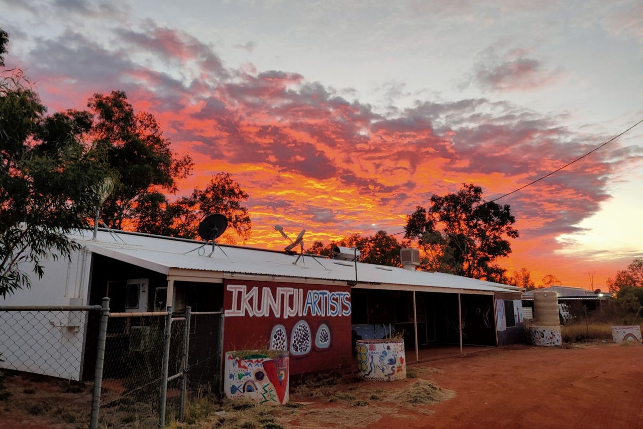 A spray painted sign is positioned on a wire fence next to a metal shed