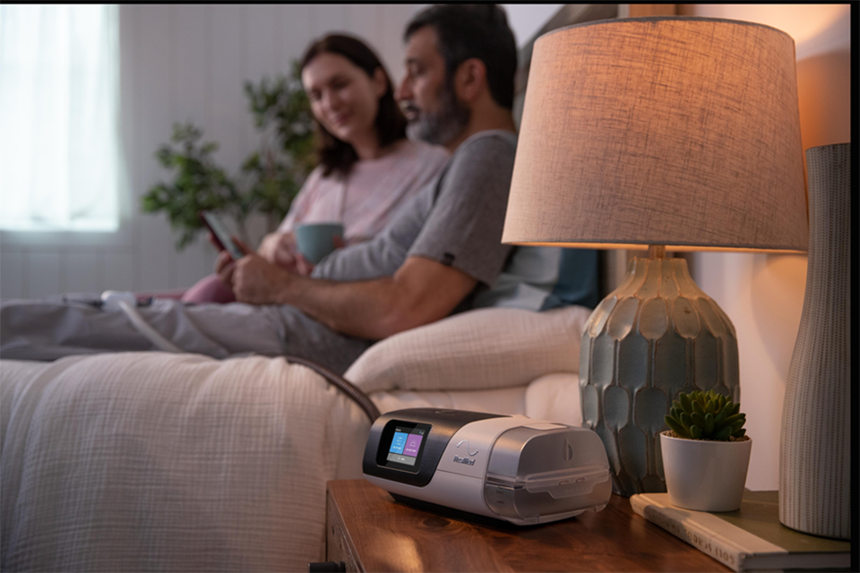 Couple sitting in bed with Resmed device on their bedside table