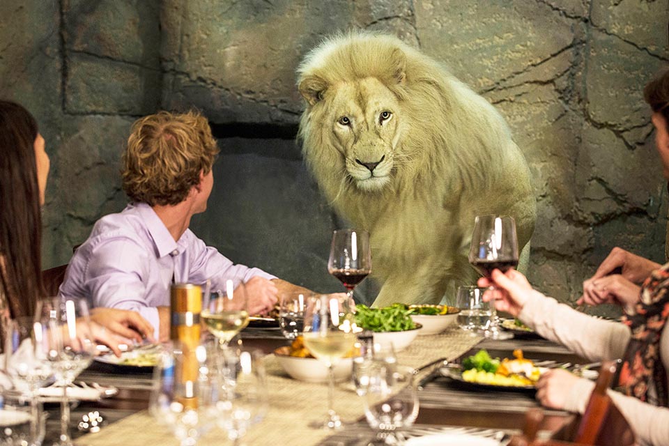 Group of diners eating a meal with a lion in the background