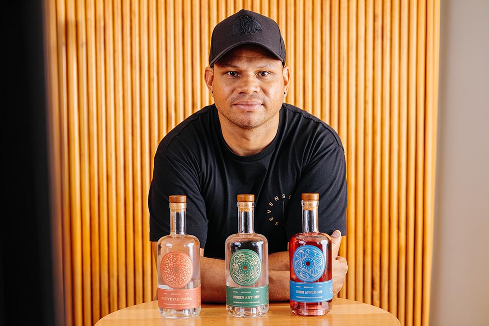 Man wearing a black cap standing at a table with 3 bottles of gin