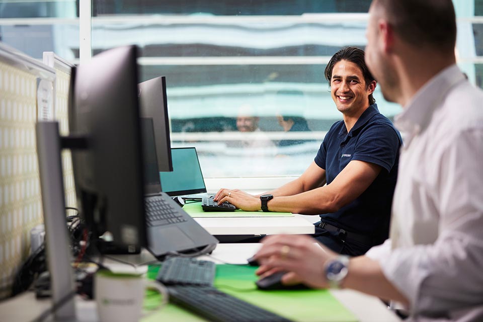 2 men working together at a shared desk with computer screen