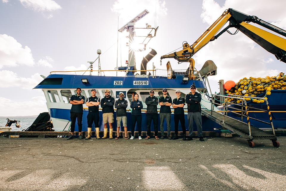 Crew of tuna fishing vessel standing on a dock alongside boat with crane