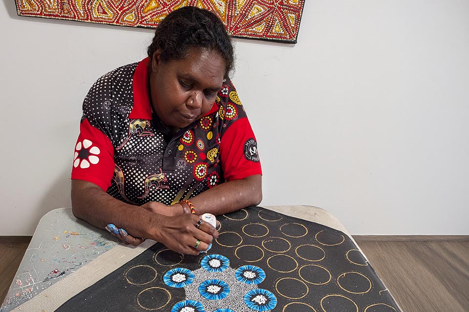 Woman creating indigenous dot painting design on canvas