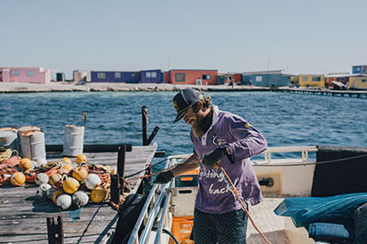 Man working on fishing boat with the shore in the distance