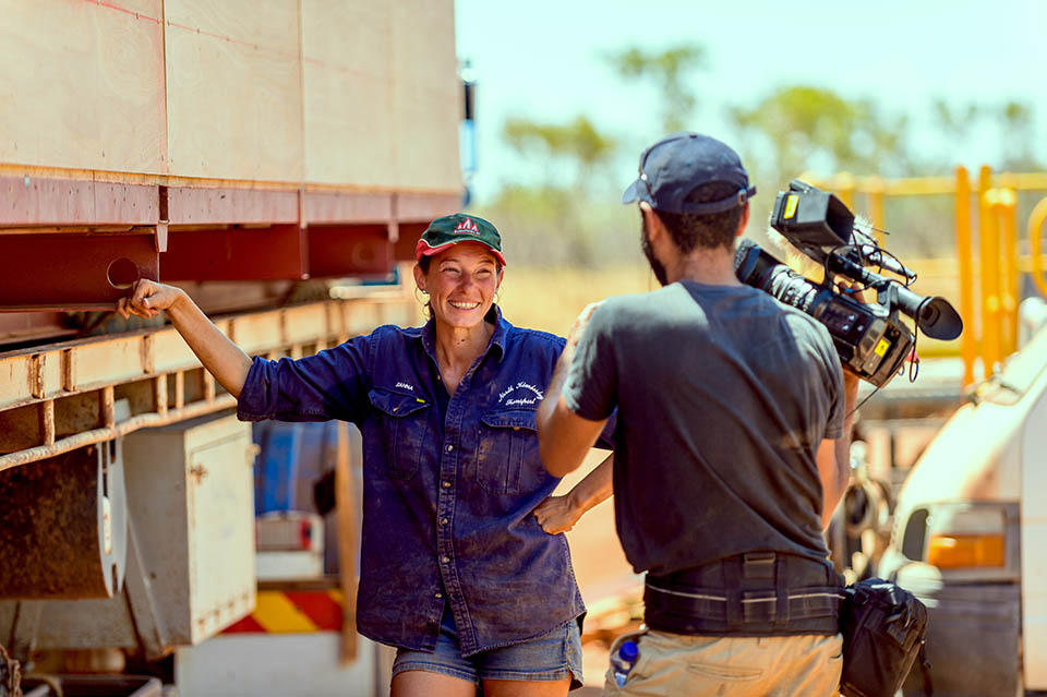 Photographer with camera capturing a woman standing alongside a semitrailer