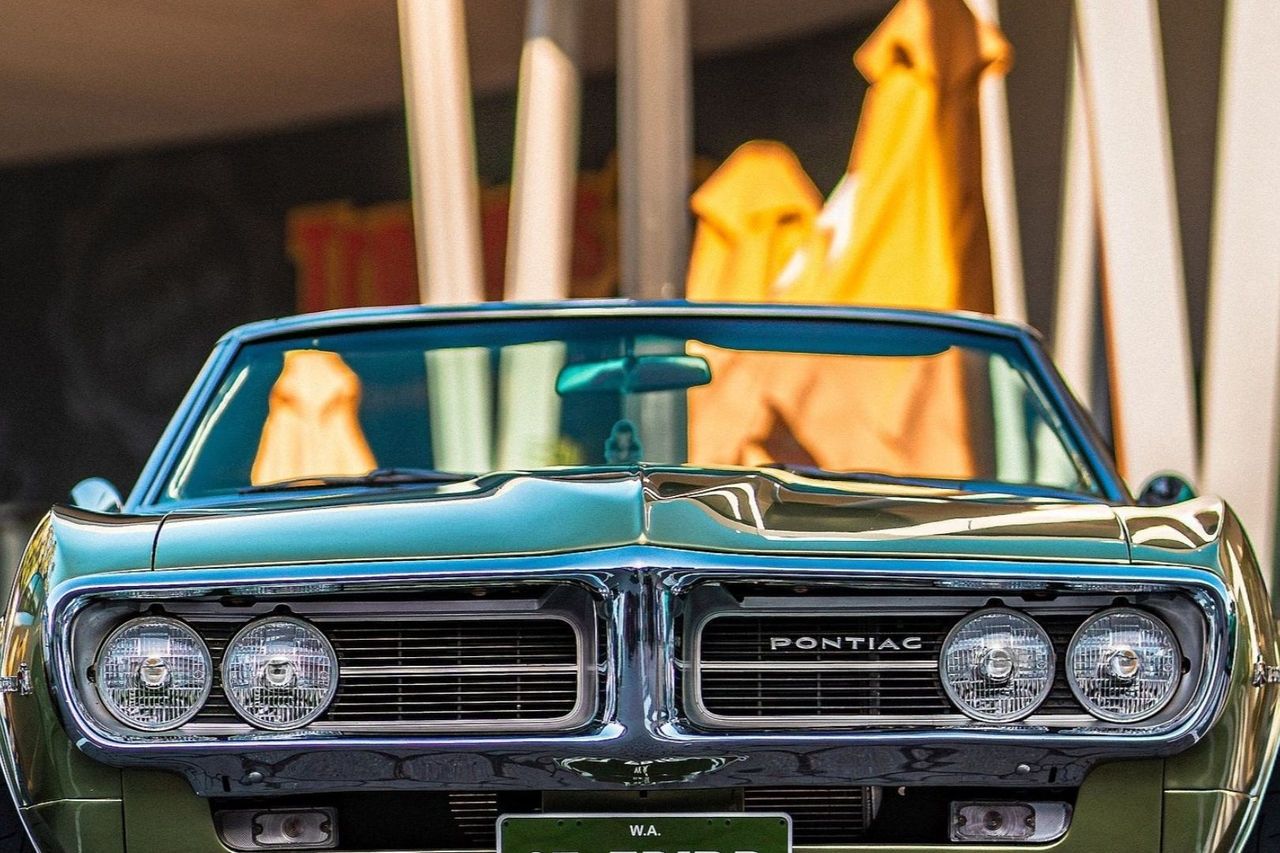 The front profile of a green 1970's American convertible car with 4 headlights