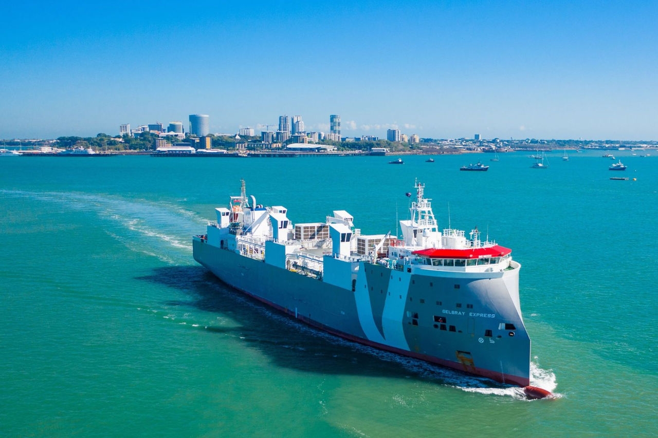 A grey and white live cattle export ship leaves a city harbour under power.