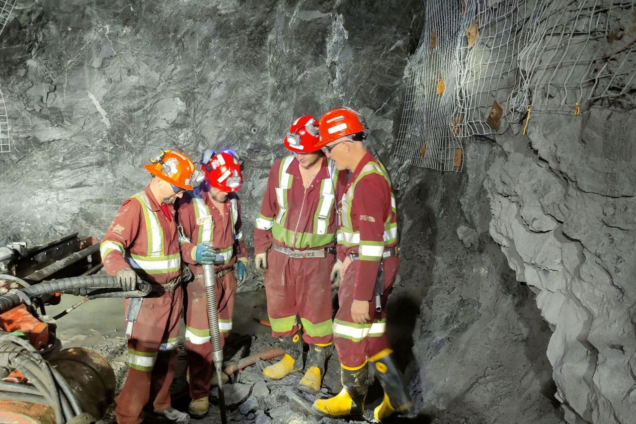 four male minors stand in a huddle in an underground mine examining some equipment