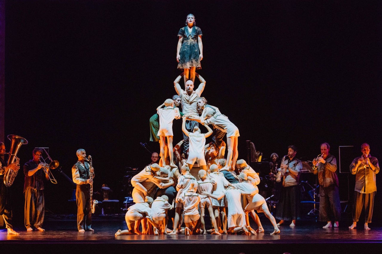 Acrobats form a human pyramid with musicians playing instruments in the background