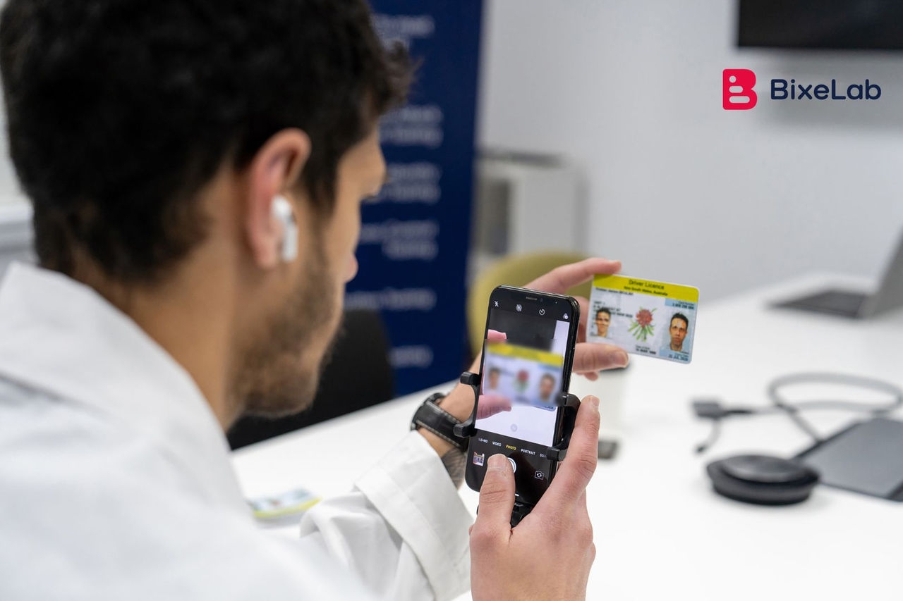 a man wearing a white lab coat takes a picture of a drivers licence using a smart phone