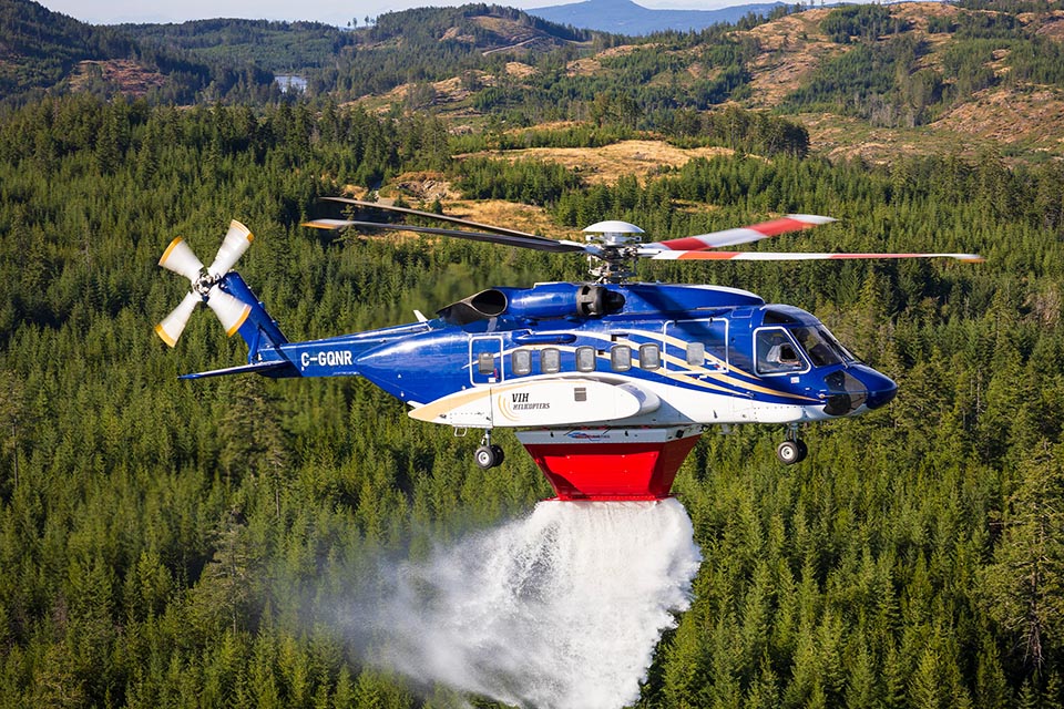 Helicoper in flight dropping water to extinguish bushfire