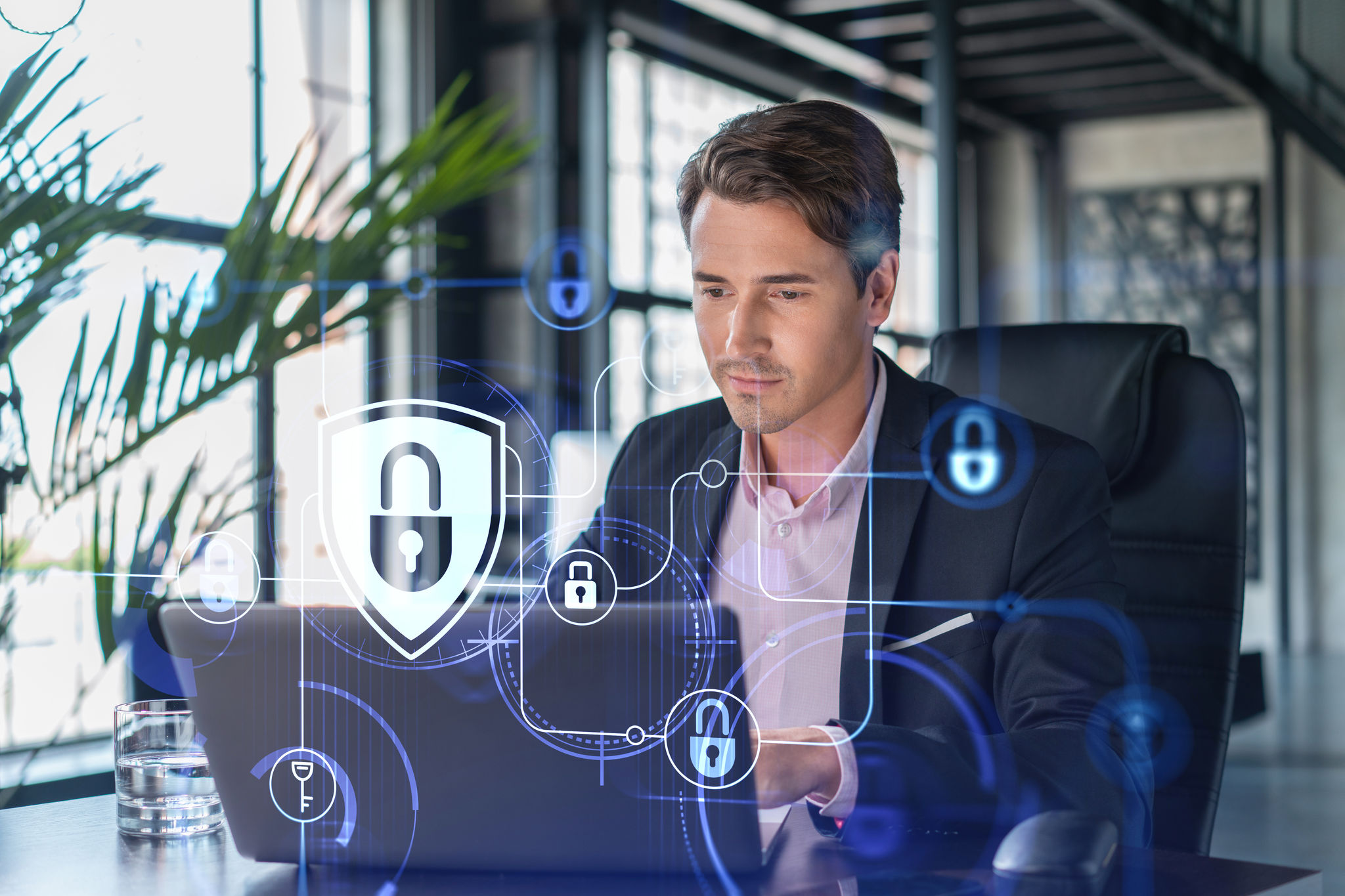 Handsome businessman in suit at workplace working with laptop to defend customer cyber security. Concept of clients information protection and brainstorm. Padlock hologram over office background.