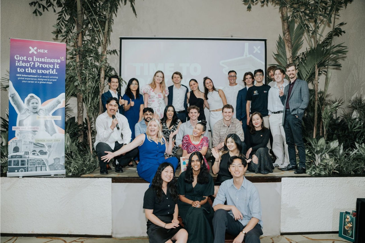 a group photo of men and women in front of a projection screen on a wall with a banner to their left