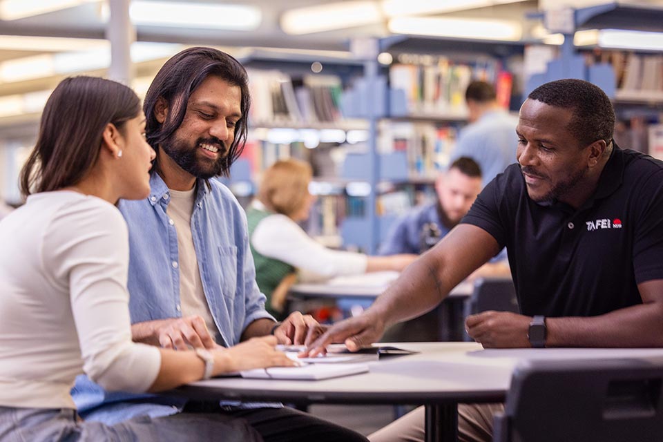 3 students sitting at a table in a library