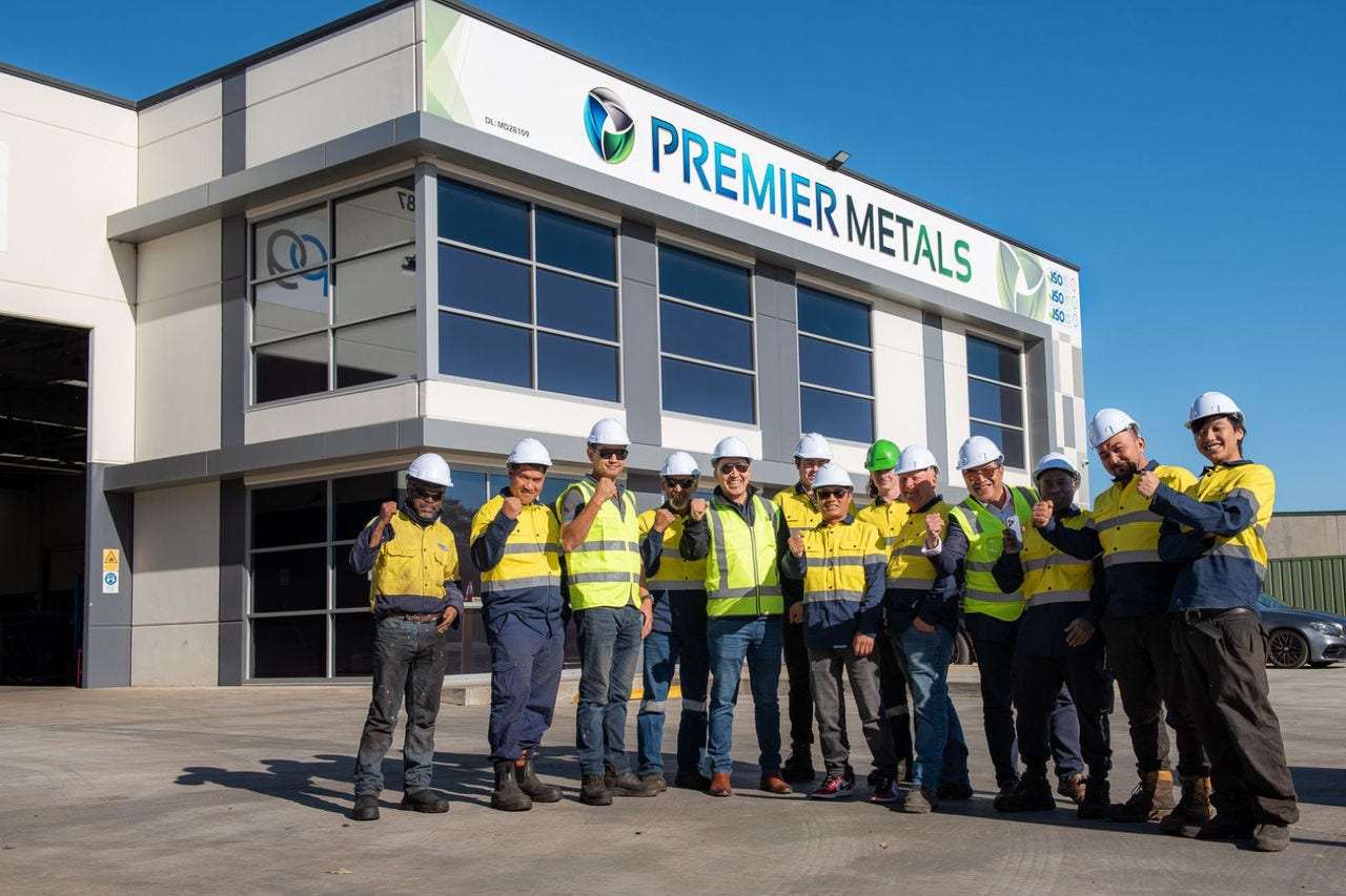 a group of men wearing yellow high visibility tops stand in front of a factory building