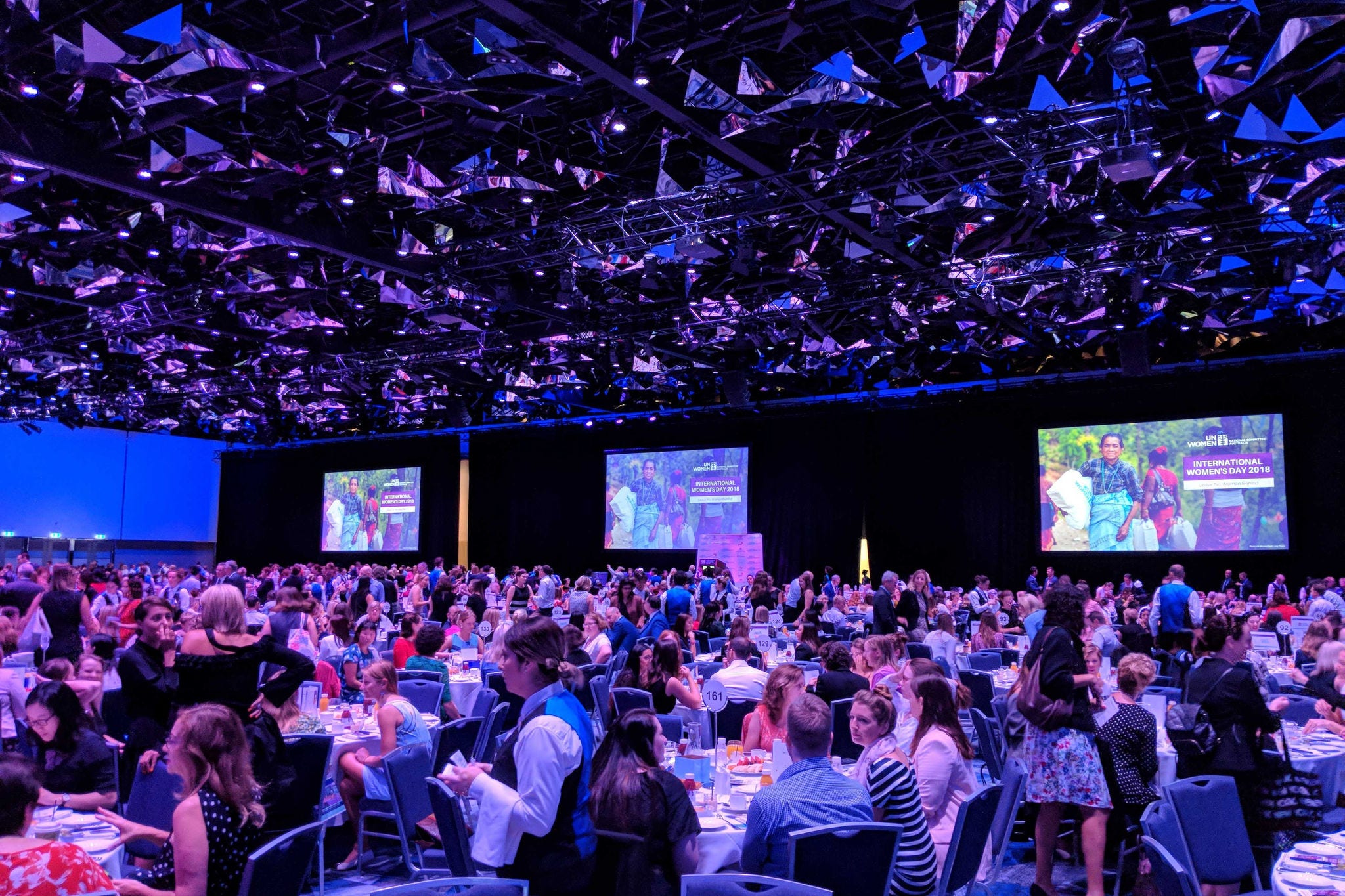 Attendees seated at a UN gala dinner event with blue lighting. 