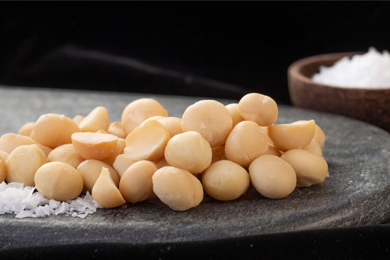 Macadamia nuts sitting on a round, natural stone serving plate with a bowl of salt in the background