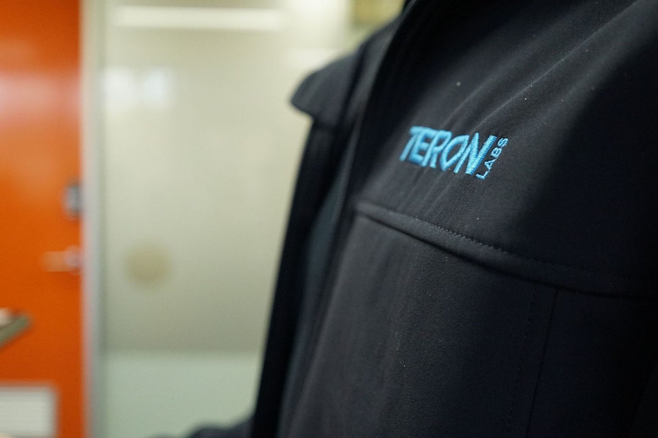 the chest of a person wearing a black top with words embroidered on the front in light blue thread