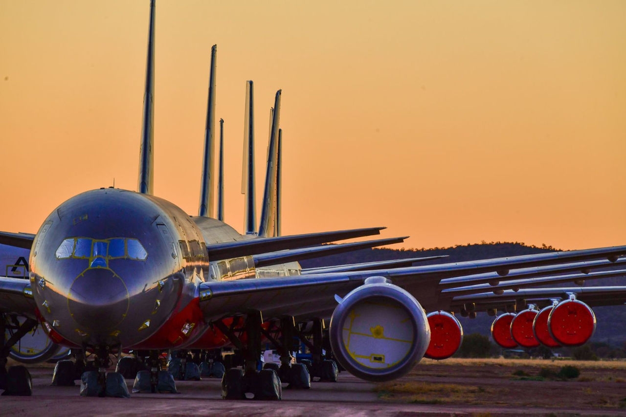 aircraft with engines covered are parked in a line with a sunset sky in the background