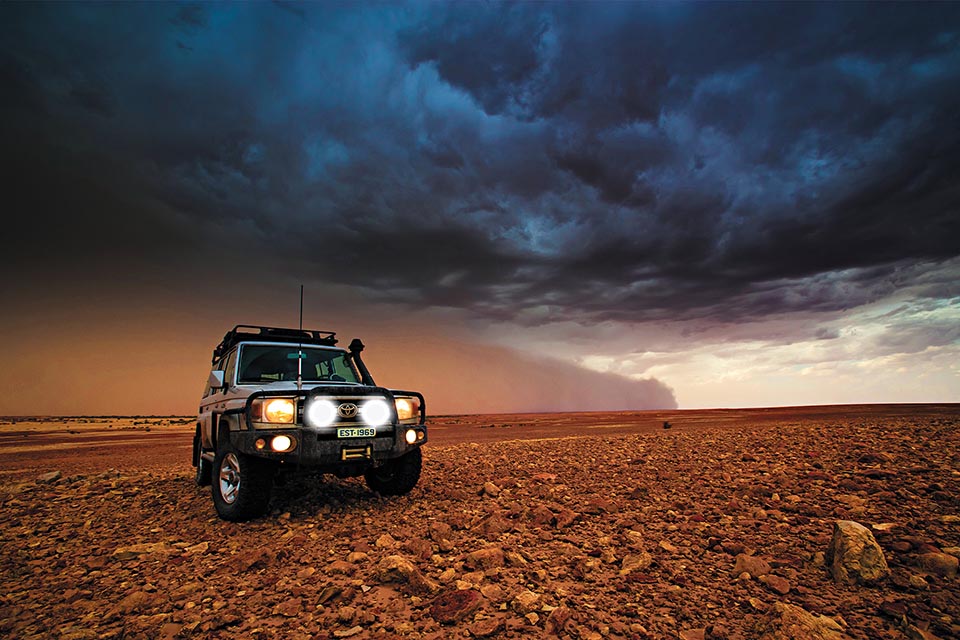 Four-wheel drive vehicle on red stoney landscape with dust storm on the horizon