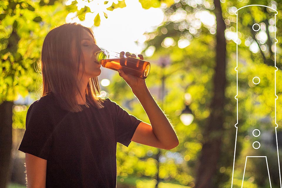 Woman drinking brown liquid from a glass bottle in a forest