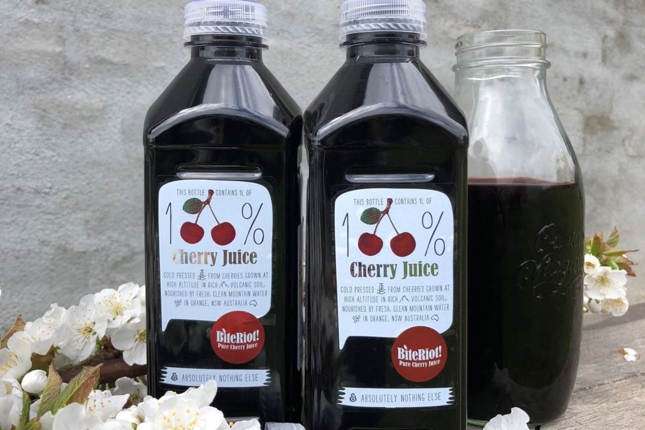 two large plastic bottles filled with red cherry juice with a half-filled glass jar